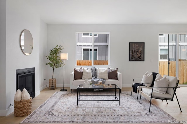 living room with baseboards, a glass covered fireplace, plenty of natural light, and wood finished floors