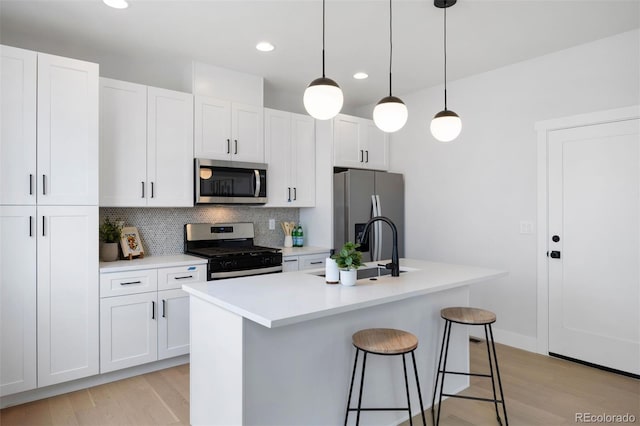 kitchen featuring light wood-type flooring, decorative backsplash, a center island with sink, and appliances with stainless steel finishes