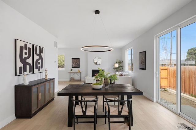dining space with light wood finished floors, a warm lit fireplace, and baseboards