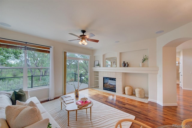 1839 Caleta Trl, Longmont, CO 80504 - living room with arched walkways, a ceiling fan, wood finished floors, and a tile fireplace