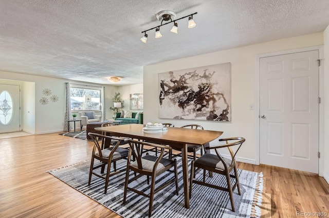 dining space featuring rail lighting, a textured ceiling, and light wood-type flooring