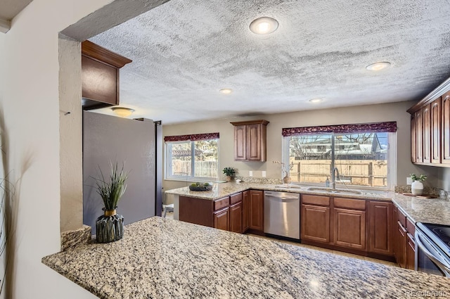 kitchen with sink, appliances with stainless steel finishes, light stone countertops, a textured ceiling, and kitchen peninsula