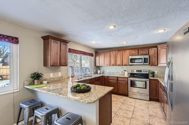 kitchen with light tile patterned flooring, a kitchen bar, light stone counters, appliances with stainless steel finishes, and kitchen peninsula