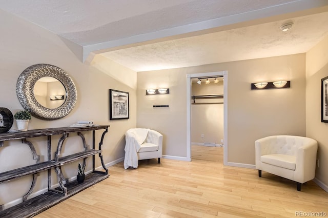 sitting room with beamed ceiling, light hardwood / wood-style floors, and a textured ceiling