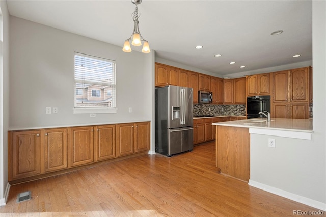 kitchen featuring pendant lighting, sink, stainless steel appliances, light hardwood / wood-style floors, and decorative backsplash