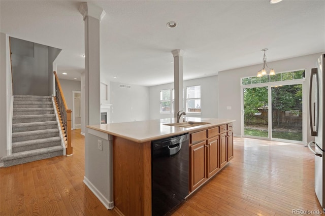 kitchen with light wood-type flooring, black dishwasher, sink, an island with sink, and an inviting chandelier