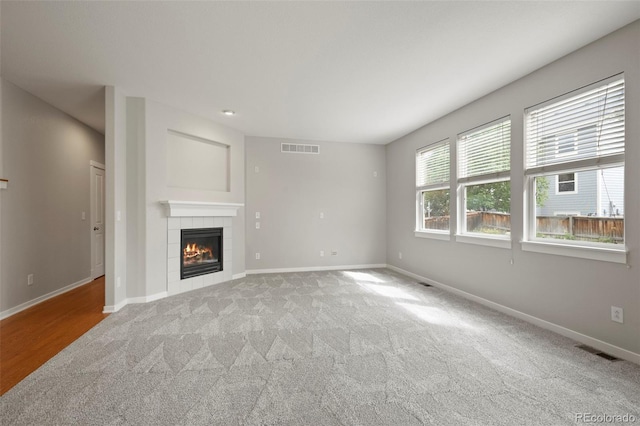 unfurnished living room with a tiled fireplace and light colored carpet