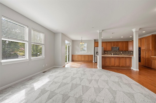 unfurnished living room with a healthy amount of sunlight, decorative columns, and light hardwood / wood-style flooring