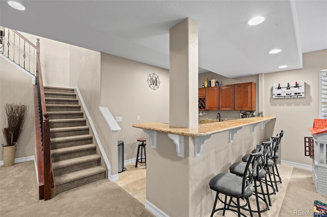 8101 Wynstone Dr, Windsor, CO 80550 - kitchen featuring brown cabinetry, a breakfast bar area, recessed lighting, light carpet, and a sink