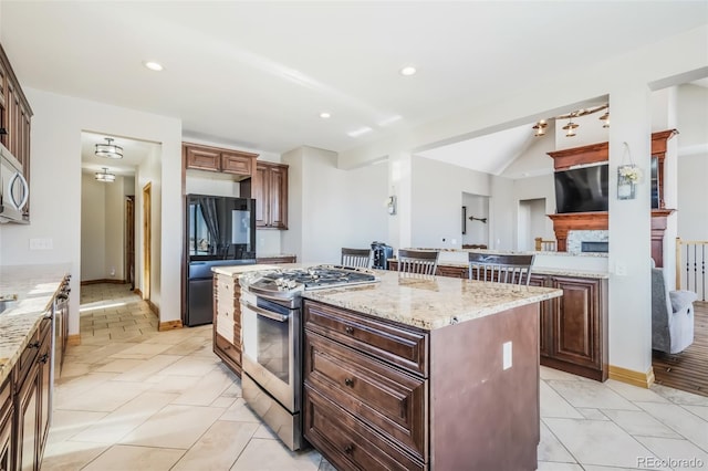 kitchen with black fridge, stainless steel gas stove, light tile patterned floors, a kitchen island, and light stone counters