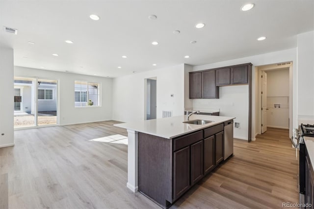 kitchen with stainless steel appliances, a kitchen island with sink, sink, and light hardwood / wood-style flooring