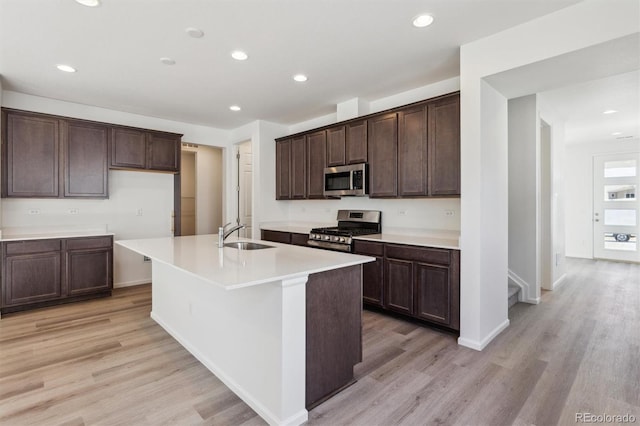 kitchen featuring appliances with stainless steel finishes, a kitchen island with sink, sink, and light hardwood / wood-style flooring