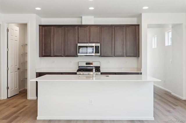 kitchen with dark brown cabinetry, stainless steel appliances, light hardwood / wood-style floors, and a center island with sink