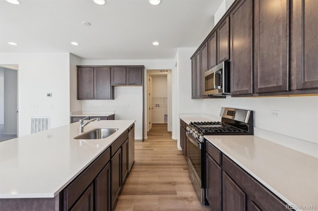 kitchen with an island with sink, sink, light hardwood / wood-style floors, stainless steel appliances, and dark brown cabinets