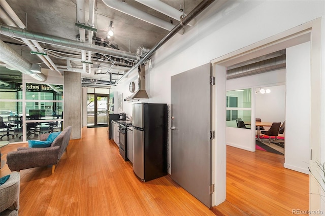 kitchen with stainless steel appliances, wall chimney range hood, and hardwood / wood-style flooring