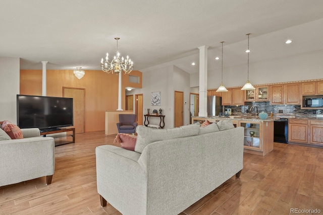 living room with light hardwood / wood-style floors, ornate columns, high vaulted ceiling, and a chandelier