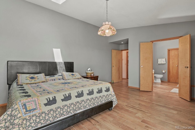 bedroom with ensuite bath, light hardwood / wood-style floors, and lofted ceiling