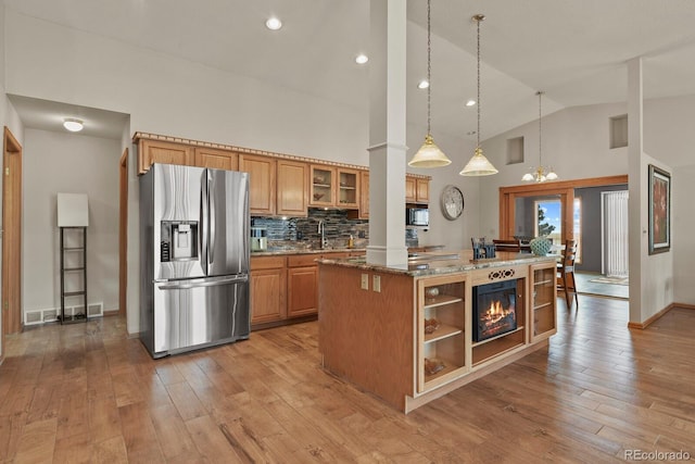 kitchen with stone counters, stainless steel fridge, decorative light fixtures, decorative backsplash, and a kitchen island