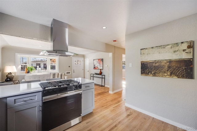 kitchen featuring gray cabinets, island exhaust hood, stainless steel range with gas stovetop, and light hardwood / wood-style floors