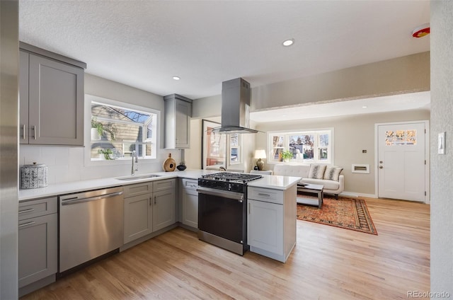 kitchen featuring sink, gray cabinetry, island range hood, appliances with stainless steel finishes, and kitchen peninsula