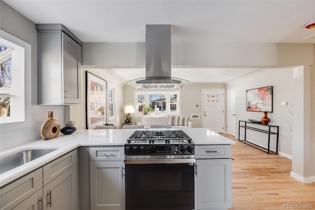 kitchen with gas stove, light hardwood / wood-style flooring, kitchen peninsula, gray cabinets, and island exhaust hood