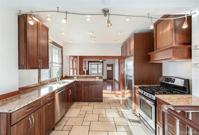 kitchen with light stone counters, kitchen peninsula, custom exhaust hood, appliances with stainless steel finishes, and sink