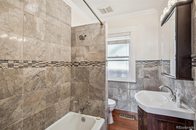 full bathroom with toilet, tile walls, tiled shower / bath combo, ornamental molding, and vanity