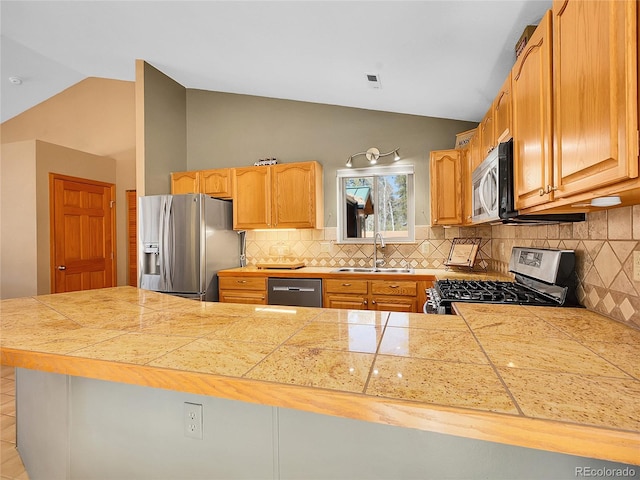 kitchen with a sink, tasteful backsplash, tile countertops, appliances with stainless steel finishes, and vaulted ceiling