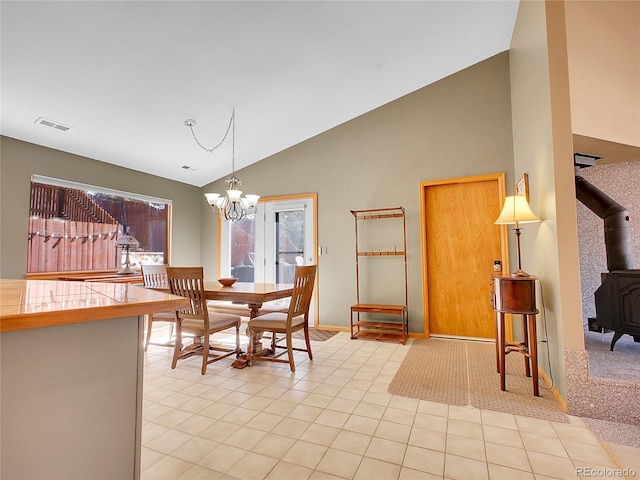 dining room with visible vents, light tile patterned floors, a wood stove, a notable chandelier, and high vaulted ceiling