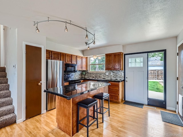 380 S 25th Ave, Brighton, CO 80601 - kitchen with black appliances, a breakfast bar, decorative backsplash, a center island, and light wood-style floors