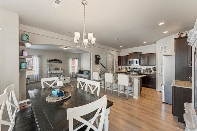 dining area with light wood finished floors, visible vents, arched walkways, and recessed lighting