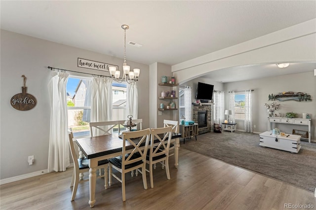 dining room featuring wood finished floors, visible vents, a fireplace, arched walkways, and baseboards