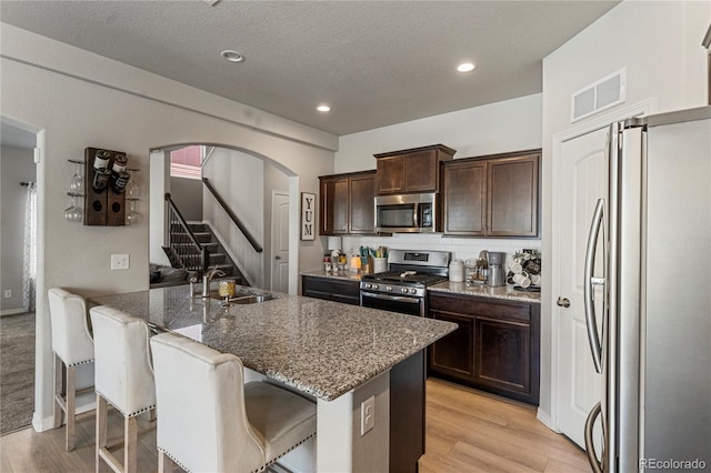 kitchen featuring a sink, a kitchen island with sink, visible vents, stone counters, and appliances with stainless steel finishes