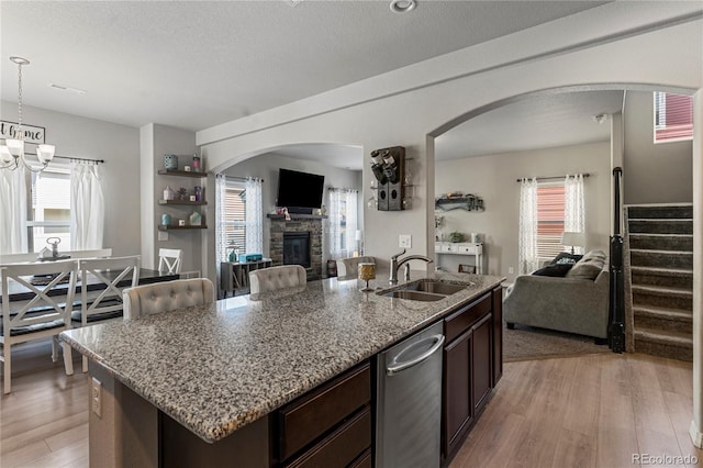 kitchen with dark brown cabinets, light stone counters, light wood finished floors, a sink, and open floor plan
