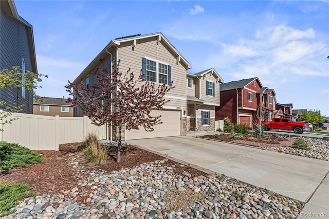 view of front facade featuring fence, an attached garage, stone siding, a residential view, and concrete driveway