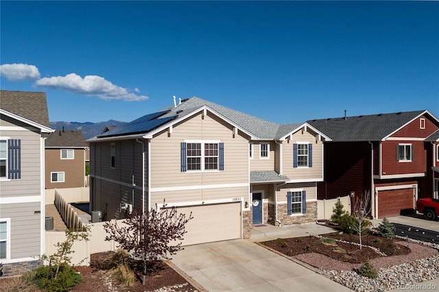 view of front facade with an attached garage, stone siding, fence, concrete driveway, and solar panels