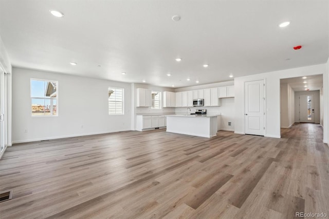 unfurnished living room with recessed lighting, light wood-style flooring, and baseboards