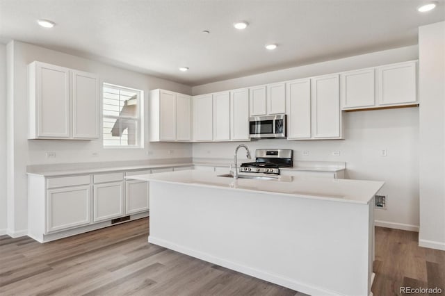 kitchen with an island with sink, light wood-style flooring, stainless steel appliances, light countertops, and white cabinets