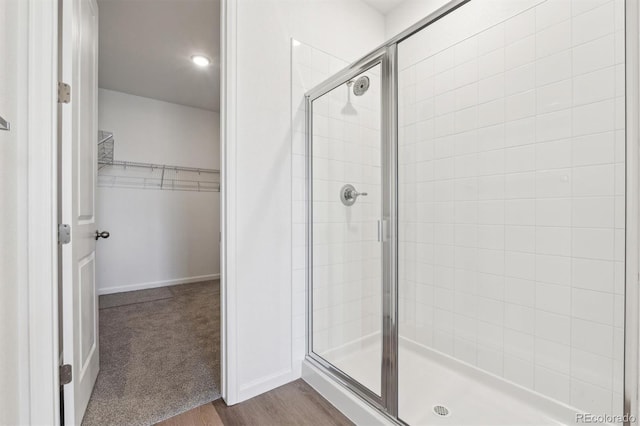 full bathroom featuring wood finished floors, baseboards, a walk in closet, and a stall shower