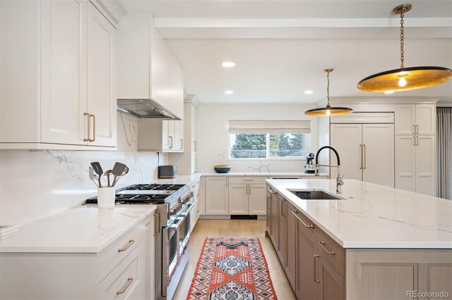 kitchen featuring premium appliances, a sink, white cabinets, light stone countertops, and pendant lighting