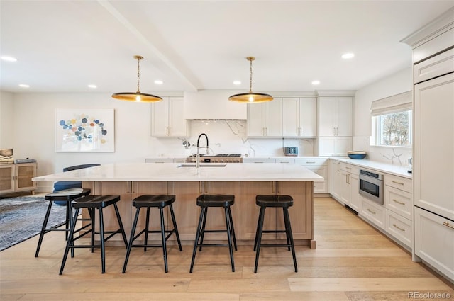 kitchen with a sink, white cabinets, a kitchen breakfast bar, hanging light fixtures, and a center island with sink