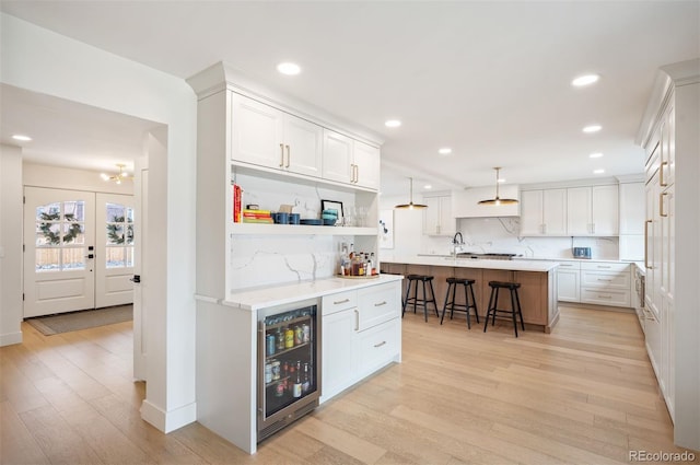 kitchen with wine cooler, light countertops, hanging light fixtures, an island with sink, and a kitchen bar