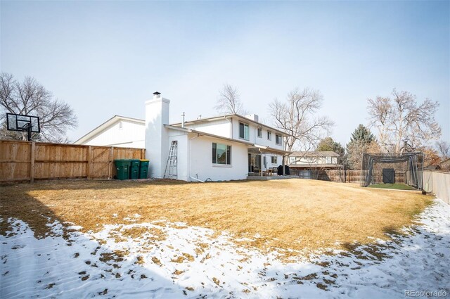 snow covered rear of property with fence and a chimney