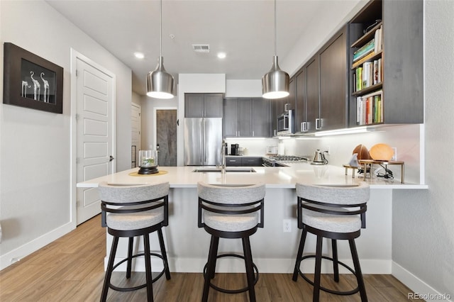 kitchen with dark brown cabinetry, decorative light fixtures, a kitchen breakfast bar, kitchen peninsula, and stainless steel appliances