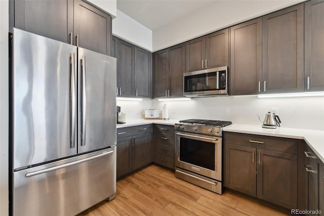 kitchen with appliances with stainless steel finishes, light hardwood / wood-style floors, and dark brown cabinets