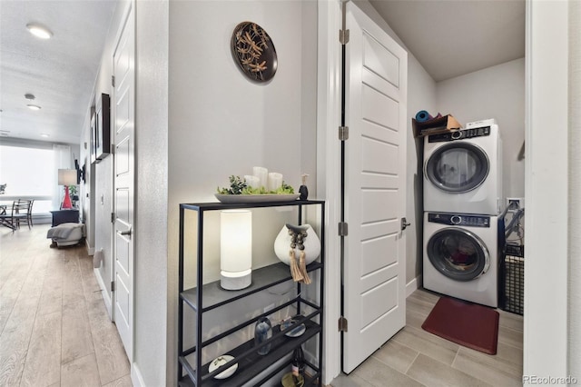 clothes washing area featuring stacked washer / drying machine, light hardwood / wood-style floors, and a textured ceiling