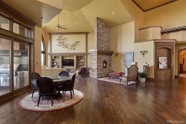 dining area with a stone fireplace, ceiling fan, hardwood / wood-style floors, and high vaulted ceiling