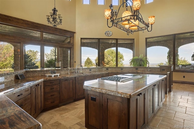 kitchen featuring sink, a center island, hanging light fixtures, stainless steel gas cooktop, and a towering ceiling