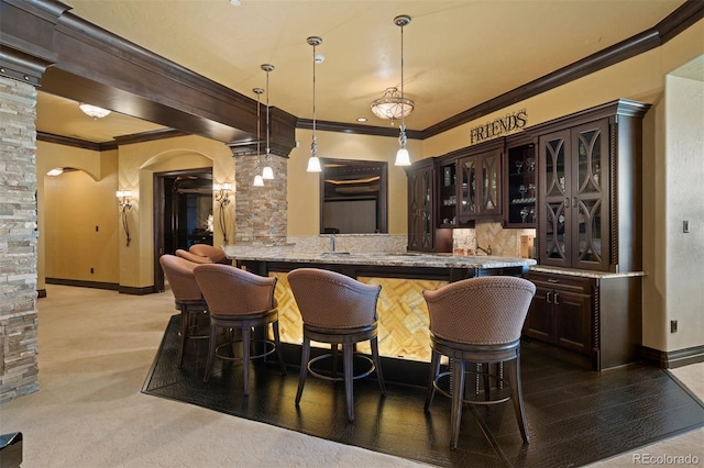 bar with pendant lighting, dark brown cabinetry, light colored carpet, and ornamental molding