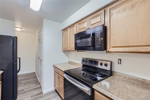 kitchen with light countertops, a textured ceiling, light brown cabinetry, light wood-type flooring, and black appliances